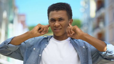 Afro-Amerikalı genç adam sokak gürültüsü yaşıyor, kulaklarını parmaklarıyla kapatıyor.