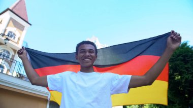 Mutlu Afro-Amerikalı genç erkek Almanya bayrağı taşıyor ve gülümsüyor, vatanseverler yürüyor