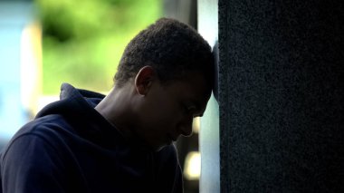 Bunalımlı Afro-Amerikan genci dışarıda oturmuş duvara yaslanıyor, kriz geçiriyor.