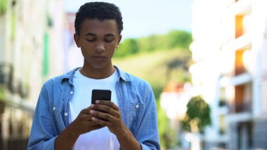 Afro-Amerikalı genç erkek dışarıda akıllı telefonlarla sohbet ediyor, internet üzerinden iletişim kuruyor.