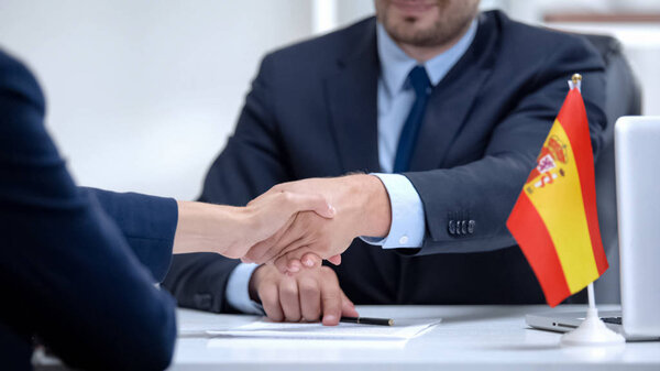 Spanish boss signing employment contract with immigrant employee, shaking hand