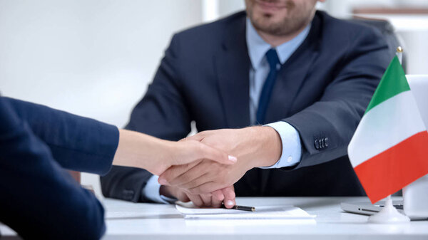Italian boss signing employment contract with immigrant employee, shaking hand