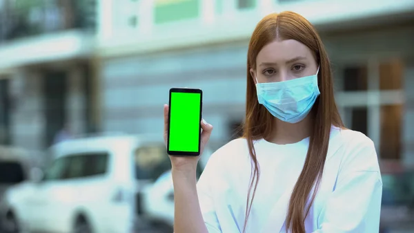 Girl in sick mask holding green screen phone, appointment with doctor online