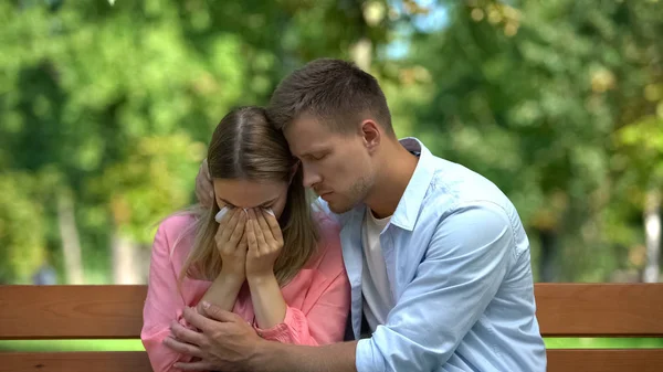Man hugging supporting crying wife in park, family togetherness, couple care