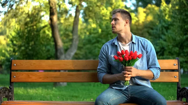 忧心忡忡的男人带着郁金香在公园的长椅上等女朋友 — 图库照片