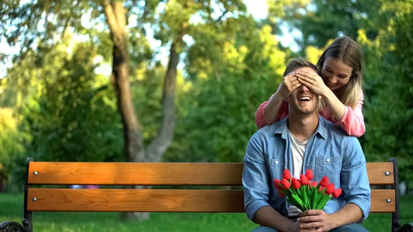 Dziewczyna Zamykając Oczy Chłopaka Czeka Bukietem Kwiatów Parku Niespodzianka — Zdjęcie stockowe