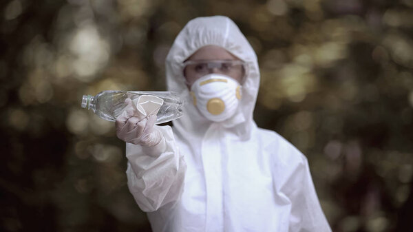 Biochemist holding crumpled plastic bottle and cup, abandoned dangerous place