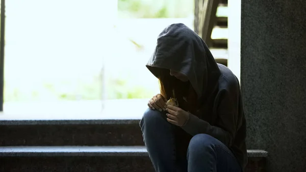 フード付きの若いホームレスの女性がサンドイッチを食べる屋外 貧困と問題 ストックフォト