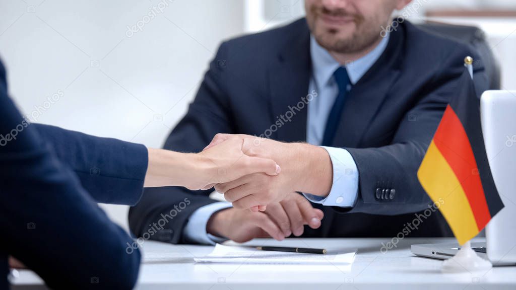 German boss signing employment contract with immigrant employee, shaking hand