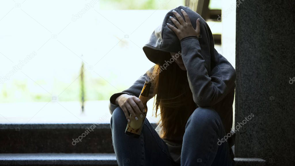 Depressed teenage girl drinking bottled beer on stairs, loneliness, addiction