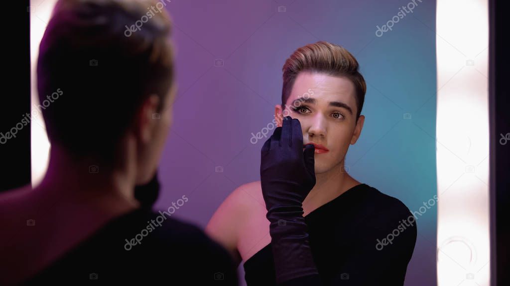 Trans man looking at half-face makeup in mirror, accepting female inner self