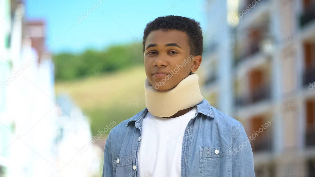 Upset afro-american teen boy in foam cervical collar sadly sighing on cam trauma