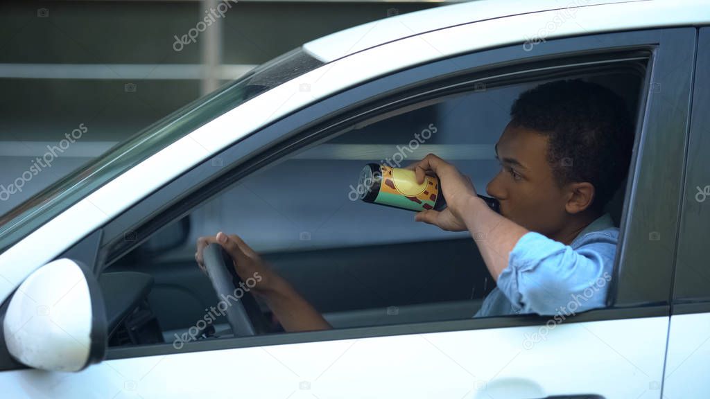Irresponsible african-american teenager drinking beer driving car, accident risk