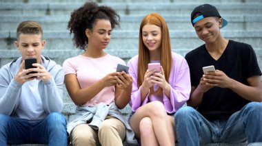Bir grup üniversite öğrencisi dışarıda oturmuş akıllı telefon oyunu oynuyor.
