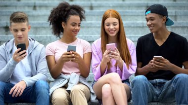 Mutlu çoklu etnik arkadaşlar dışarıda akıllı telefonlardan sosyal ağlar kuruyor.