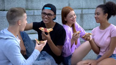 Mutlu gençler ellerinde pizza tutuyorlar yaz tatilinin tadını çıkarıyorlar, arkadaşlar boş vakit geçiriyor.