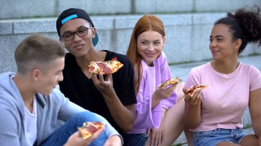 Neşeli gençler birlikte vakit geçiriyorlar dışarıda pizza yiyorlar, arkadaşlık kuruyorlar.