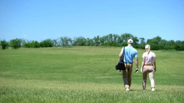 Çift erkek ve kadın golfçüler kulüpleri çanta, ders ile sahada yürüyüş