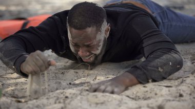 Çamurlu yüzü ağlayan, gemi enkazından kurtulan, yasadışı sınır geçişi yapan bir erkek mülteci.