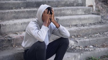 Depresyondaki genç siyahi erkek dışarıda oturuyor, duygusal taciz, aile sorunu.