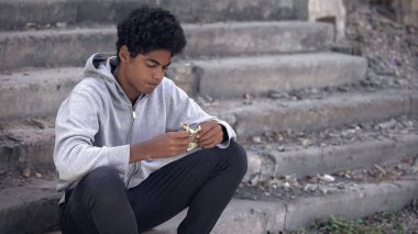 Kapüşonlu üzgün Afro-Amerikalı genç elindeki dolarlara bakıyor, işsizlik.