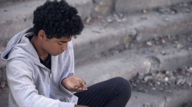 Elinde bozuk paralarla dışarıda oturan zavallı genç, şehir işsizliği.