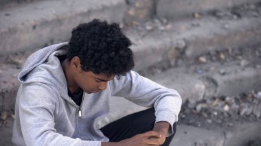 Üzgün Afro-Amerikalı çocuk merdivenlerde oturup hayattaki sorunları ve savaşı düşünüyor.