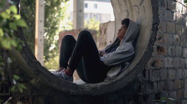 Kapüşonlu üzgün yalnız öğrenci yalnız başına oturuyor terk edilmiş bina, ergenlik izolasyonu