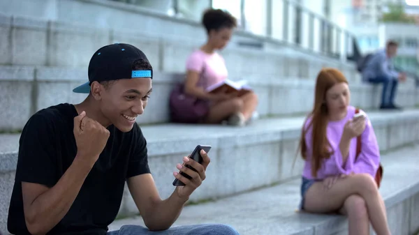 Excited black student reading smartphone message showing yes gesture, success
