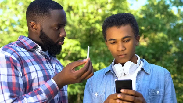 Father scolding young son playing phone, showing marijuana weed, bad habits