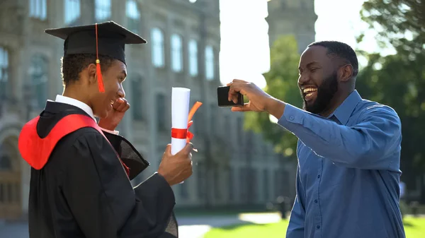 笑顔お父さん作るスマートフォンビデオの幸せな卒業生息子とともに卒業証書 イベント — ストック写真