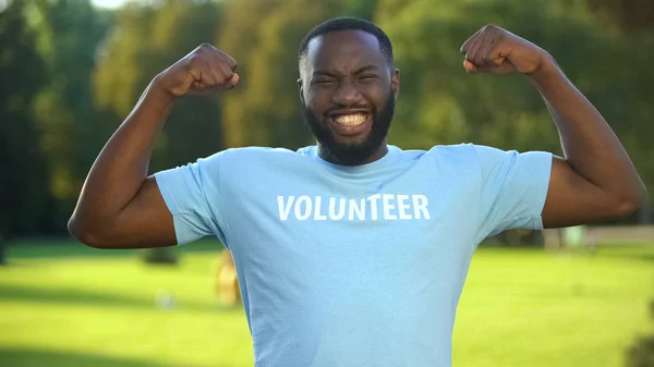 強さのジェスチャーを示す興奮したアフリカの男性ボランティアTシャツ 寄付の団結 — ストック写真