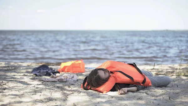 身穿救生衣的年轻女子躺在海滨 在沉船后感到身体不适 — 图库照片