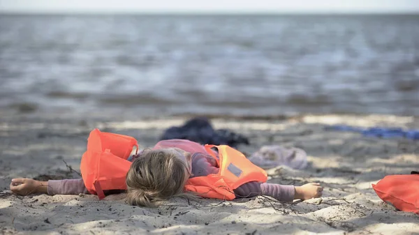 身穿救生衣的小女孩躺在海滨 是自然灾害的幸存者 — 图库照片