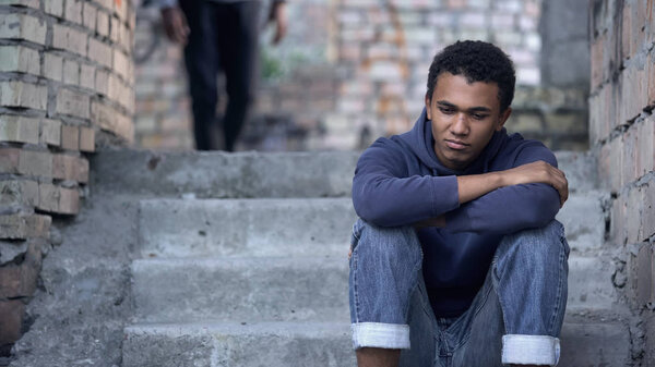 Pensive afro-american teenager sitting on stairs, misunderstanding with parents