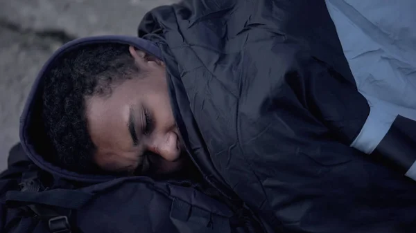 Afrikanischer Männlicher Flüchtling Liegt Mit Schlafsack Bedeckt Auf Der Straße lizenzfreie Stockfotos