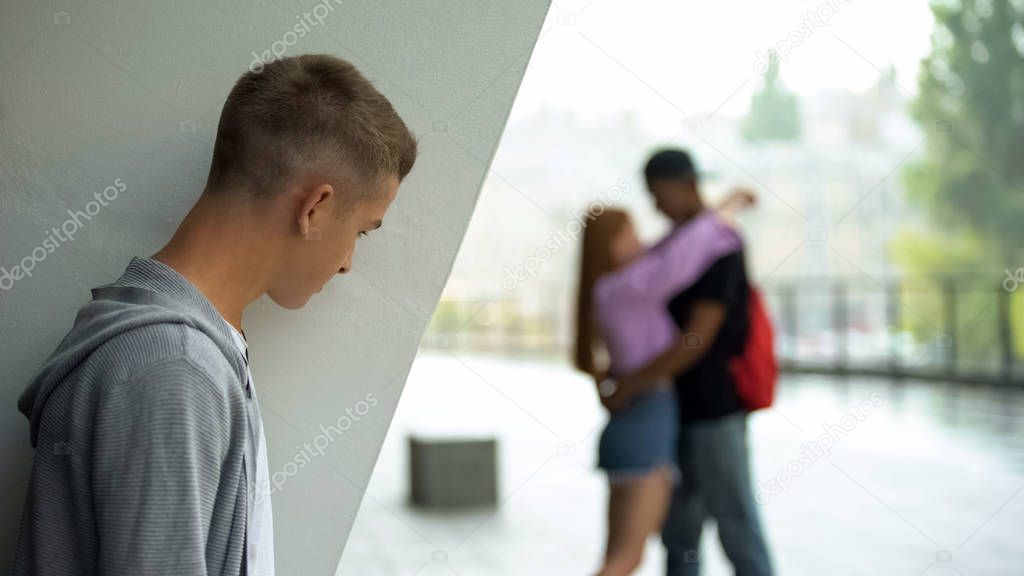 Depressed male student looking at girlfriend hugging man, love disappointment