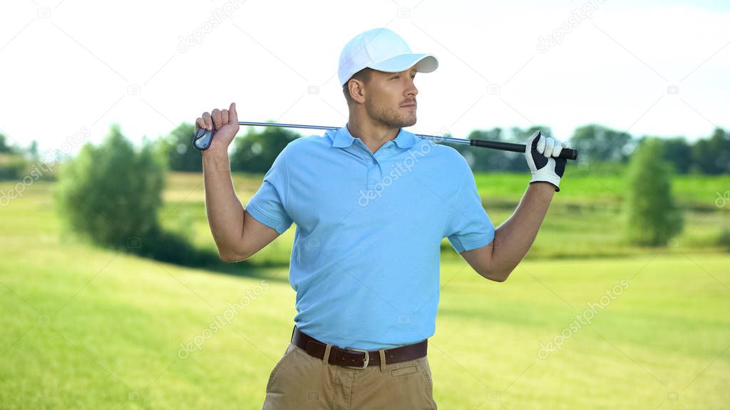 Joyful male player holding golf club behind shoulders, ready to start sport game