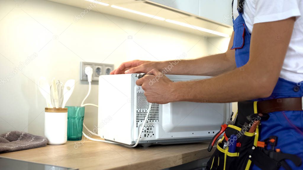 Man in uniform repairing microwave using screwdriver, maintenance guarantee