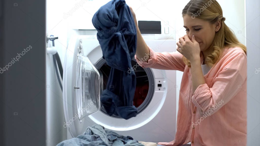 Woman closing nose from stinky clothes after washing, low-quality soap-powder