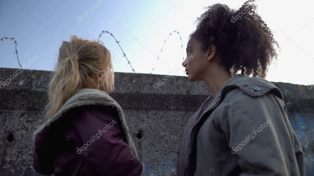 Mixed-race teenage friends looking at barbed wire fence, refugee camp, hope