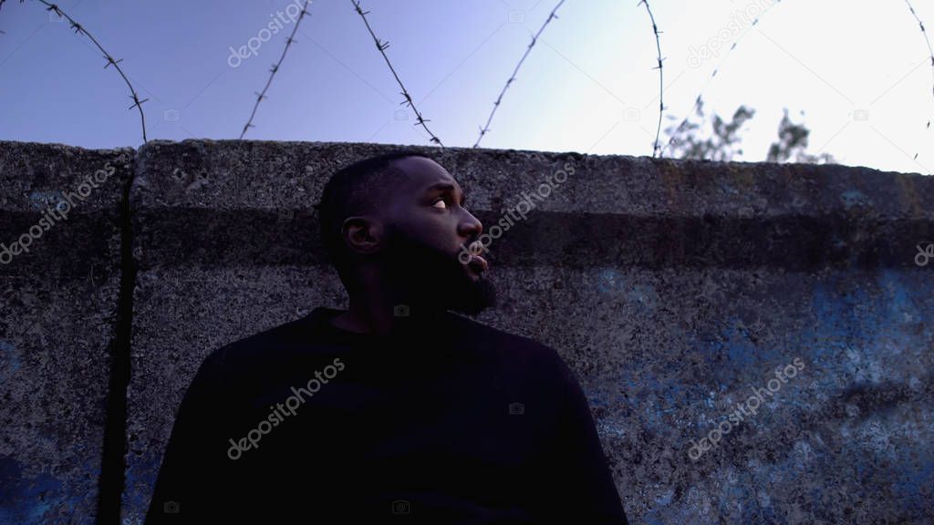 Imprisoned afro-american man looking at barbed wire, refugee camp, hopelessness