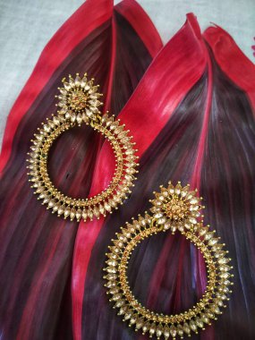 İki kırmızı yaprağın üzerinde altın renkli bir çift küpe..