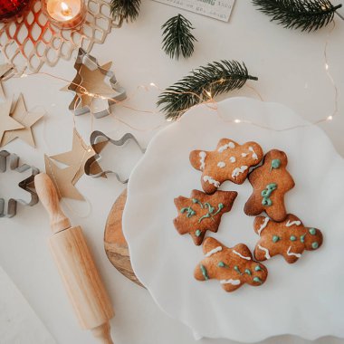 Noel ağacı şeklindeki komik ev yapımı kurabiye, kar taneleri ve beyaz tabakta beyaz bir adam, ahşap raptiyeli beyaz bir masada, Noel ağacı dalları ve çelenklerle,