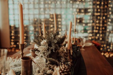 Bej ve ahşap renklerde şık bir Noel masası, altın çatal bıçaklı cam, mum, pamuk ve çelenk, sahte bir arka plan ve Noel iç mimarisine karşı