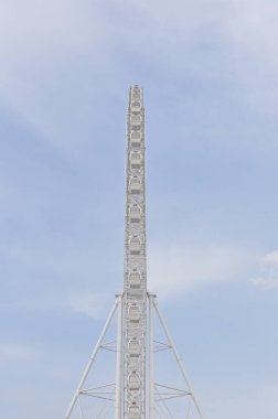 Beyaz, yüksek dönme dolabın yan tarafında açık mavi gökyüzüne karşı kapsül şeklinde kablolar var.