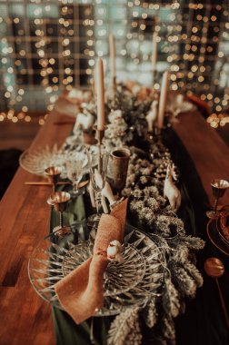 Bej ve ahşap renklerde şık bir Noel masası, altın çatal bıçaklı cam, mum, pamuk ve çelenk, sahte bir arka plan ve Noel iç mimarisine karşı