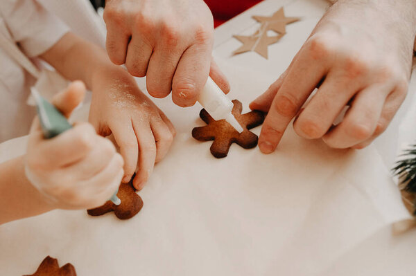 hands of mom and baby painted on cookies with food coloring on baking paper, on a white table with decor from paper stars