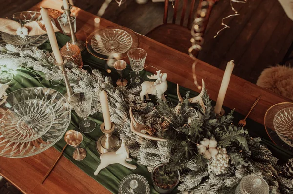 Bej ve ahşap renklerde şık bir Noel masası, altın çatal bıçaklı cam, mum, pamuk ve çelenk, sahte bir arka plan ve Noel iç mimarisine karşı
