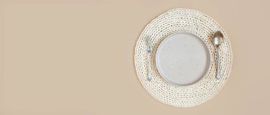 şık bej rengi tek renkli masa ayarı, boş düz yuvarlak tabak, hasırdan bir peçeteye çatal ve bıçak, metin için yeri olan pankart.